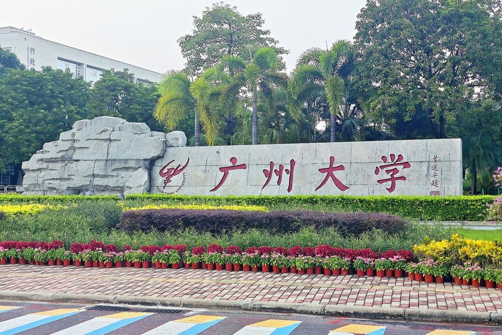 Guangzhou University's name stone in University Town, behind beds of flowers
